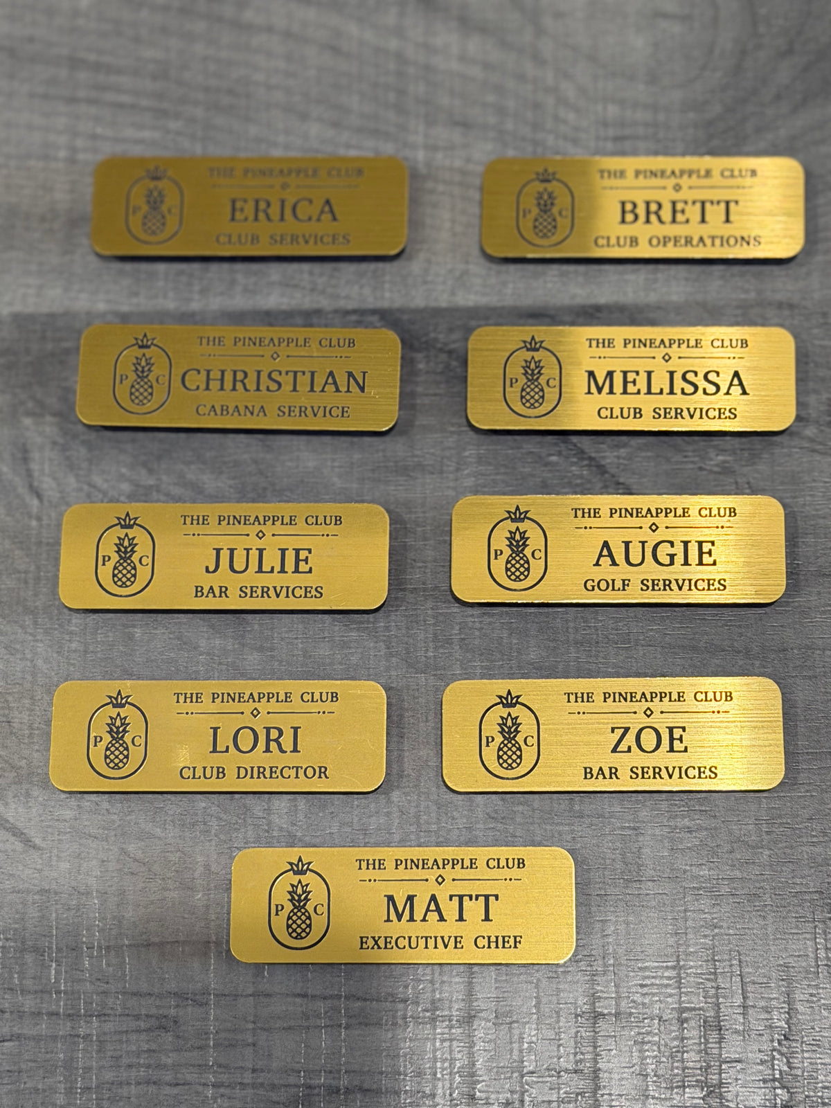 Set of yellow engraved club name badges with pineapple logo and service roles