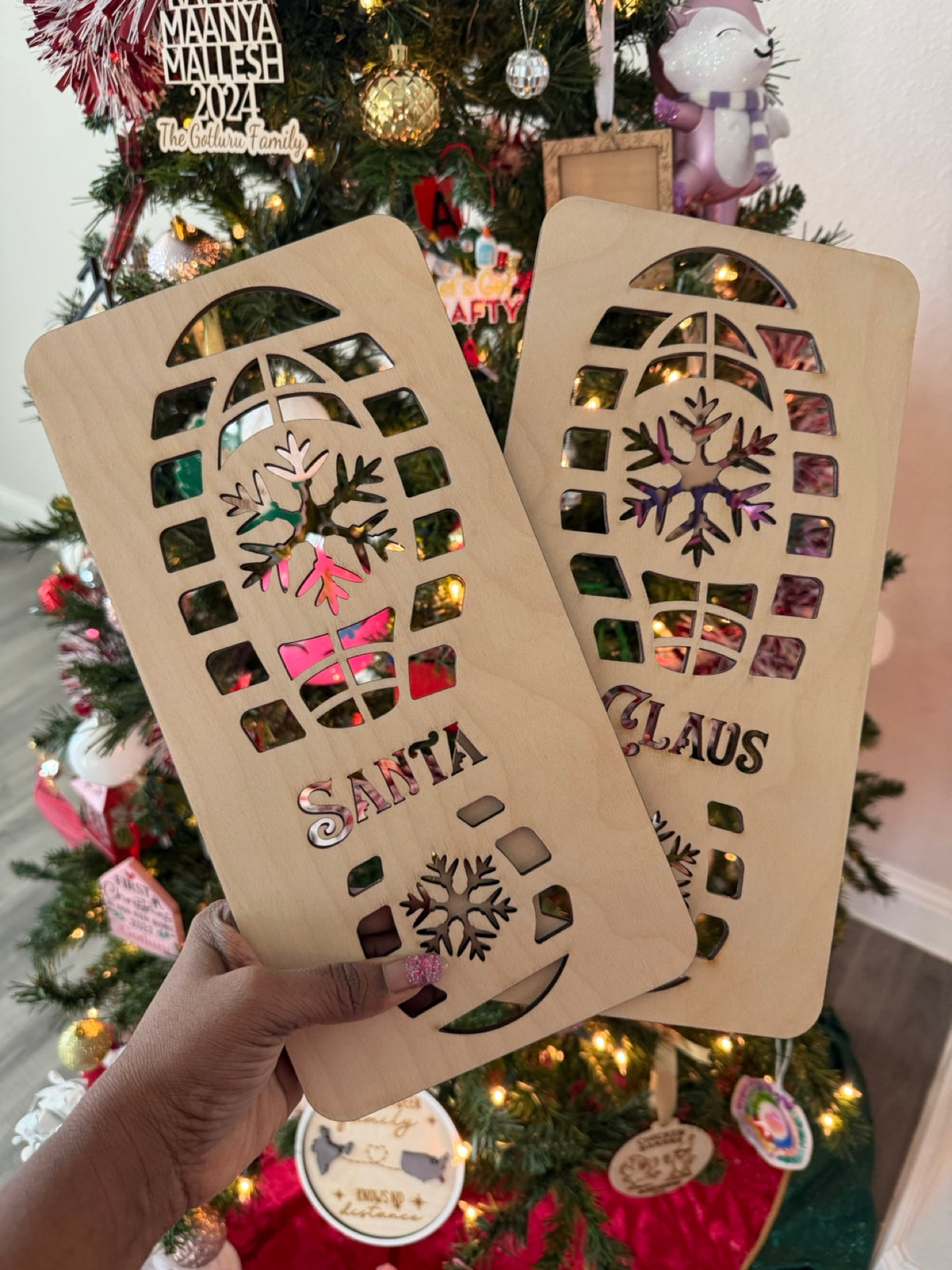 Wooden Santa footprint stencils spelling SANTA and CLAUS held up in front of a decorated Christmas tree