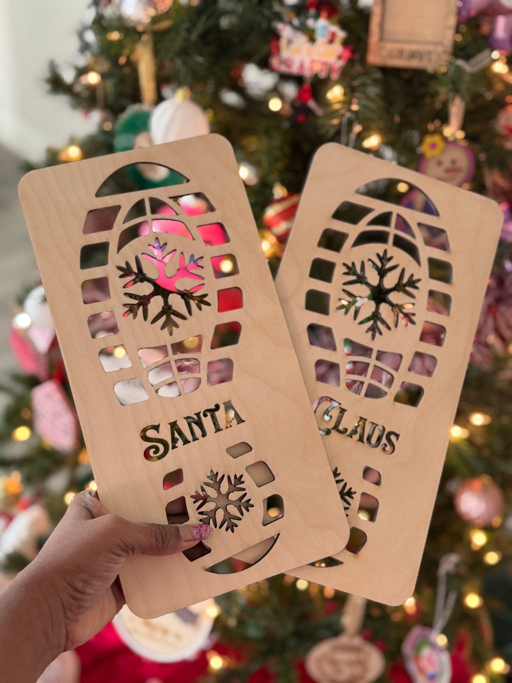 Laser-cut wooden Santa boot footprint stencils with snowflake cutouts in front of Christmas tree