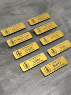 Gold engraved name badge cards with pineapple logo, names, and job titles