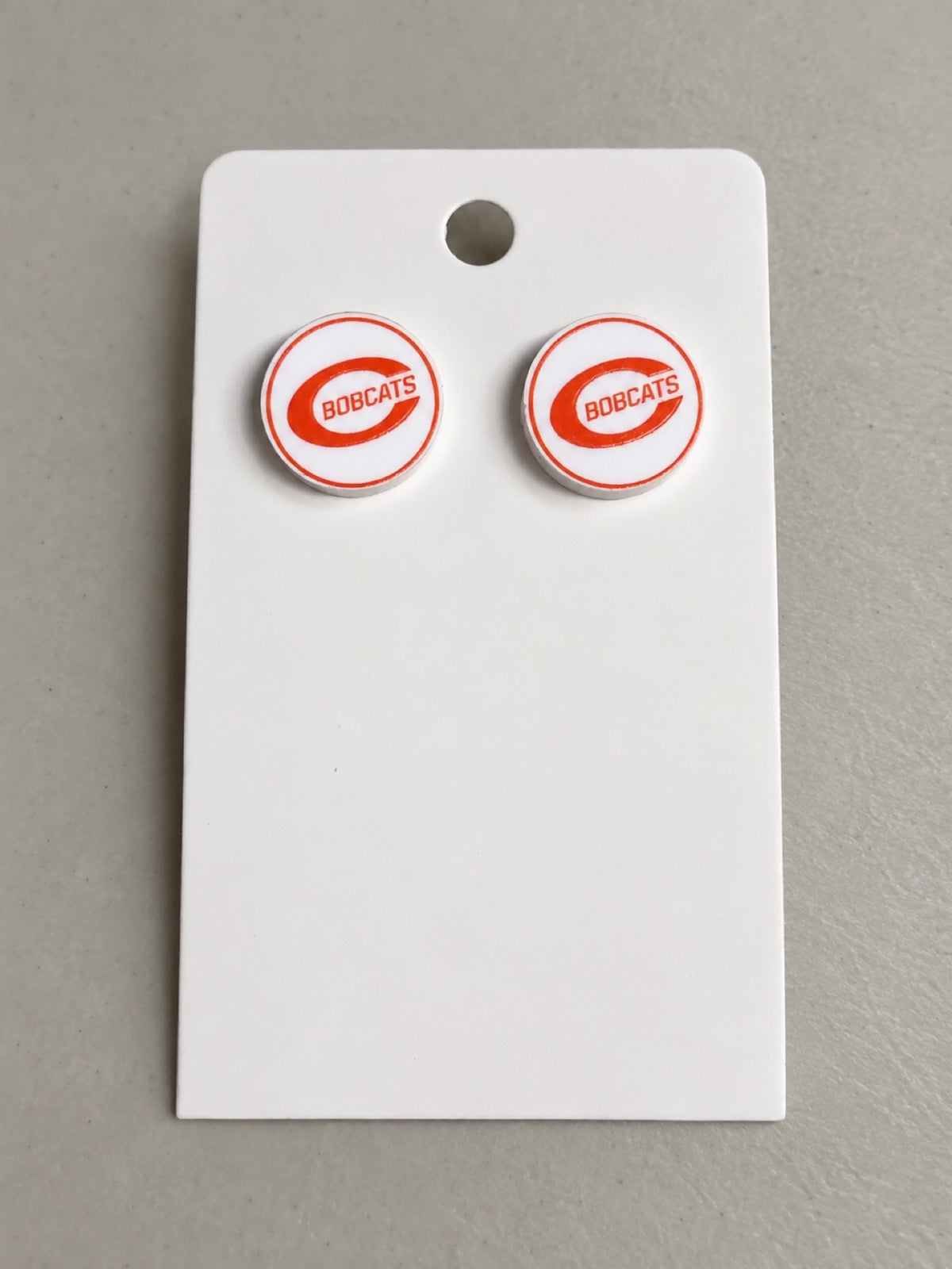 BOBCATS round acrylic stud earrings with orange Bobcats C logo on white