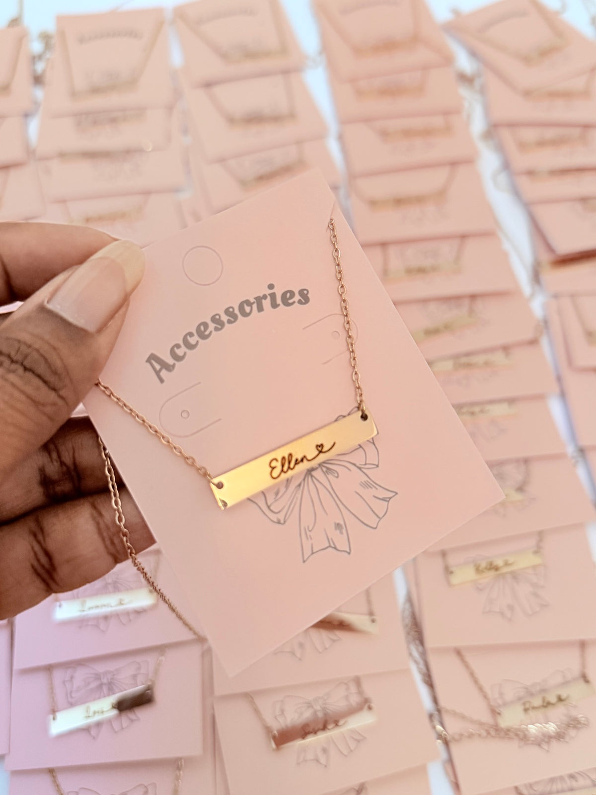 Hand holding rose gold personalized bar necklace engraved with name Ellen on pink accessories card