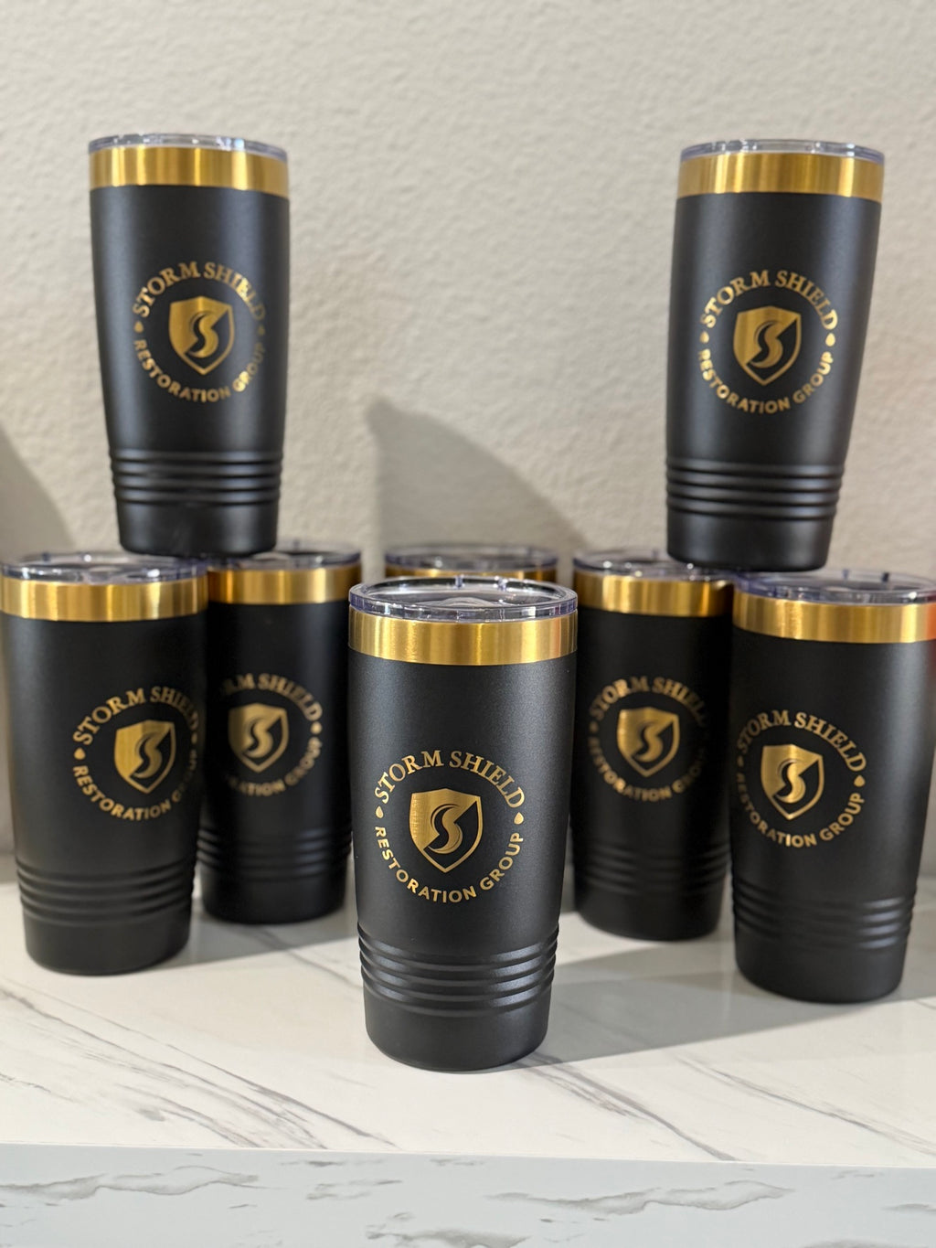 Bulk order of custom black 20oz laser-engraved tumblers with gold business logos for corporate gifts